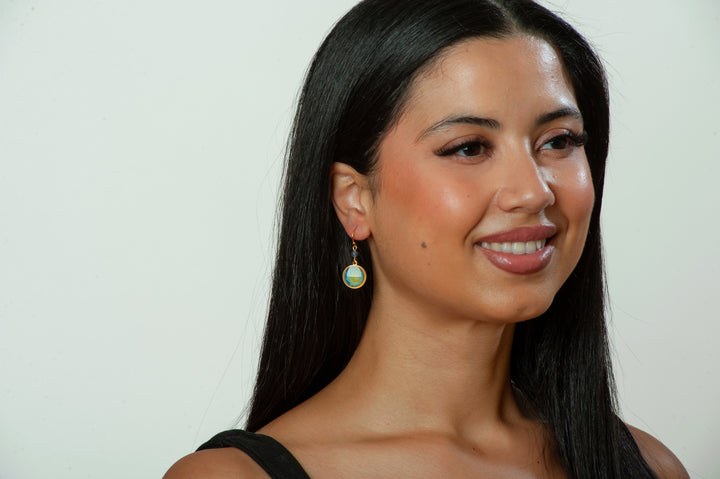 Woman with long dark hair wearing earrings against a plain background