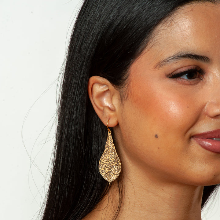 Close-up of a woman wearing gold earrings with a plain background
