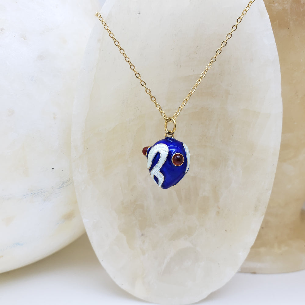 Blue and white fish pendant on a gold chain against a stone background