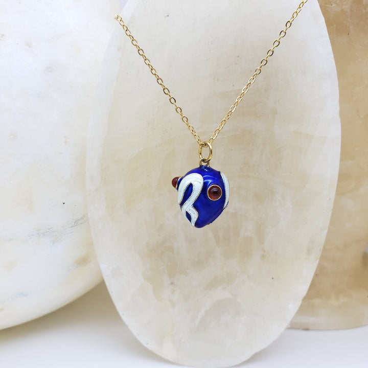 Blue and white fish pendant on a gold chain against a stone background