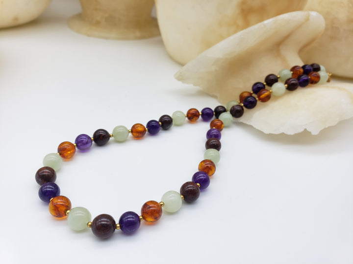 Multicolored beaded necklace on a white surface with seashells in the background
