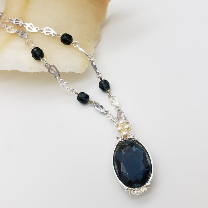 Necklace with a large blue gemstone and smaller black beads on a white background
