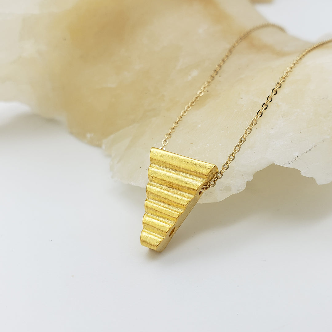 Gold necklace with a triangular pendant on a light background