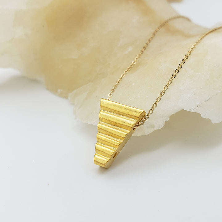 Gold necklace with a triangular pendant on a light background