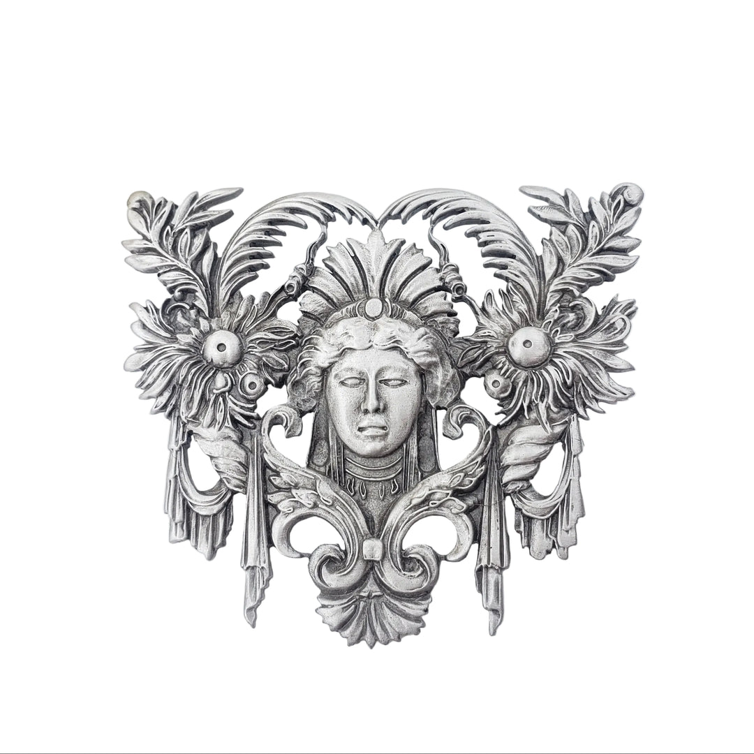 Decorative silver wall piece with floral and face design on a white background