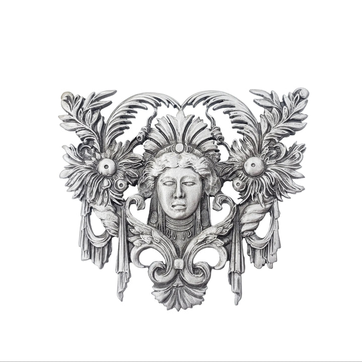 Decorative silver wall piece with floral and face design on a white background