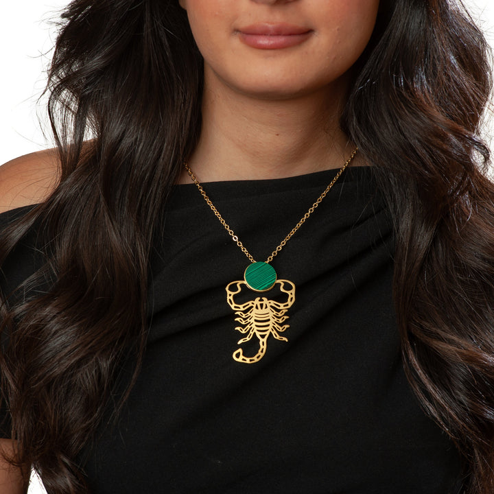 Woman wearing a black top and gold necklace with a green pendant