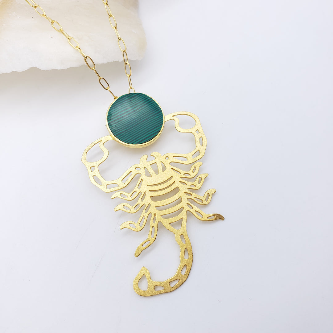 Gold scorpion-shaped pendant with a green gemstone on a light background
