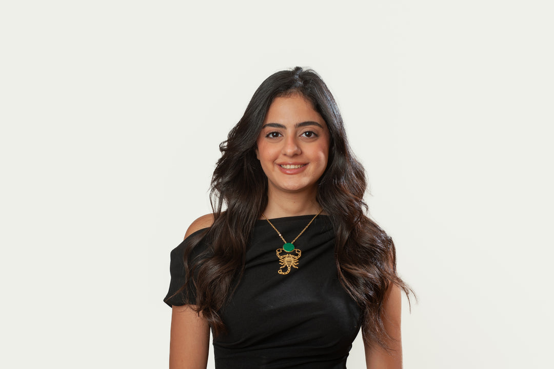 Woman wearing a black off-shoulder top with a gold scorpion pendant on a white background