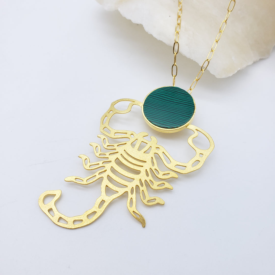 Gold scorpion-shaped pendant with a green gemstone on a white background