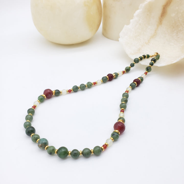 Beaded necklace with green, red, and gold beads on a white background