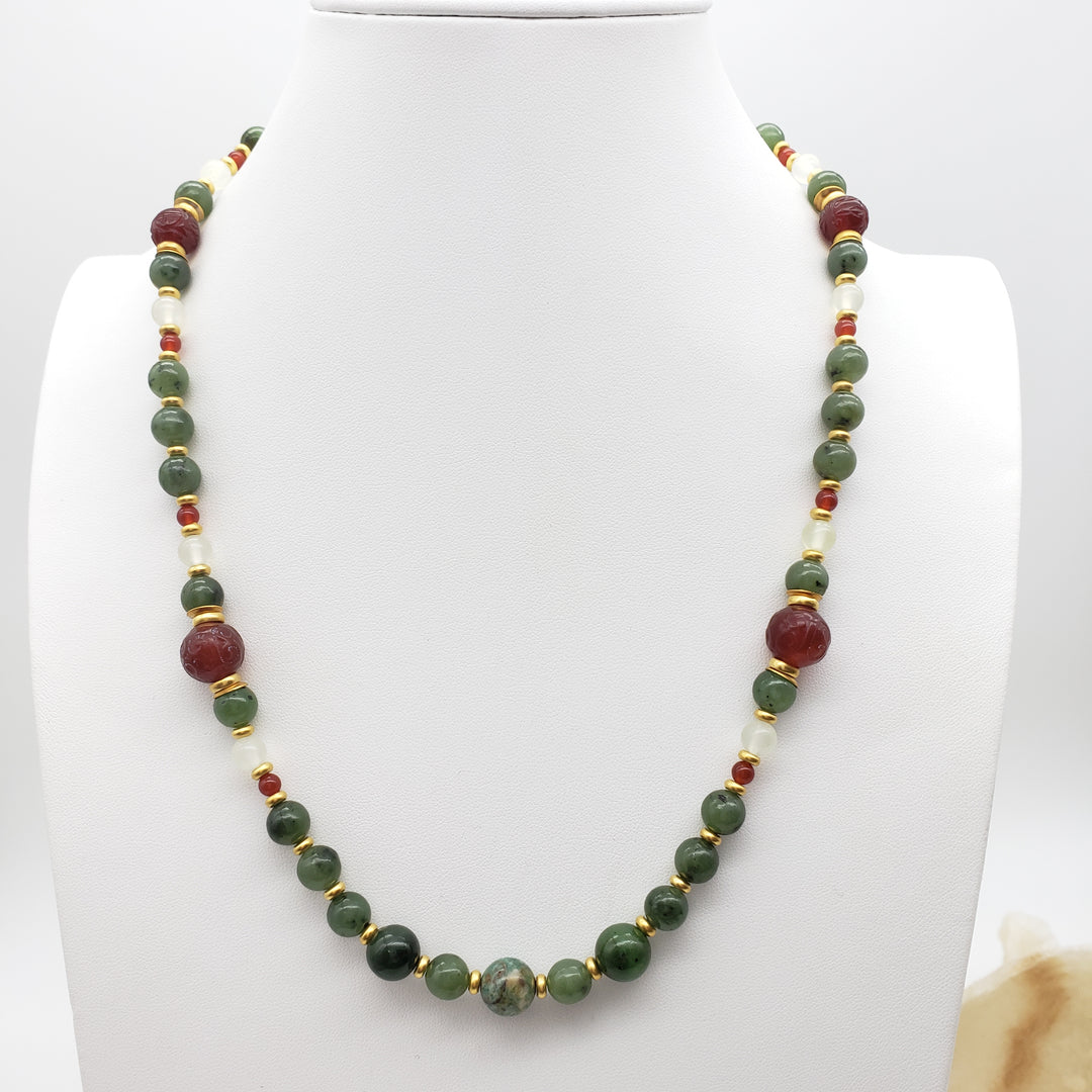 Necklace with green, red, and gold beads on a white stand