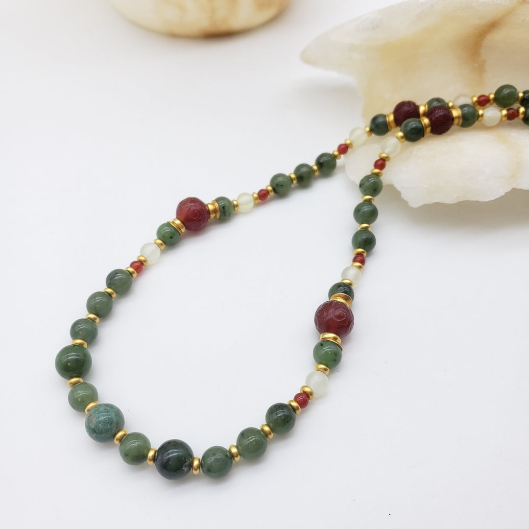 Beaded necklace with green, red, and gold beads on a white background
