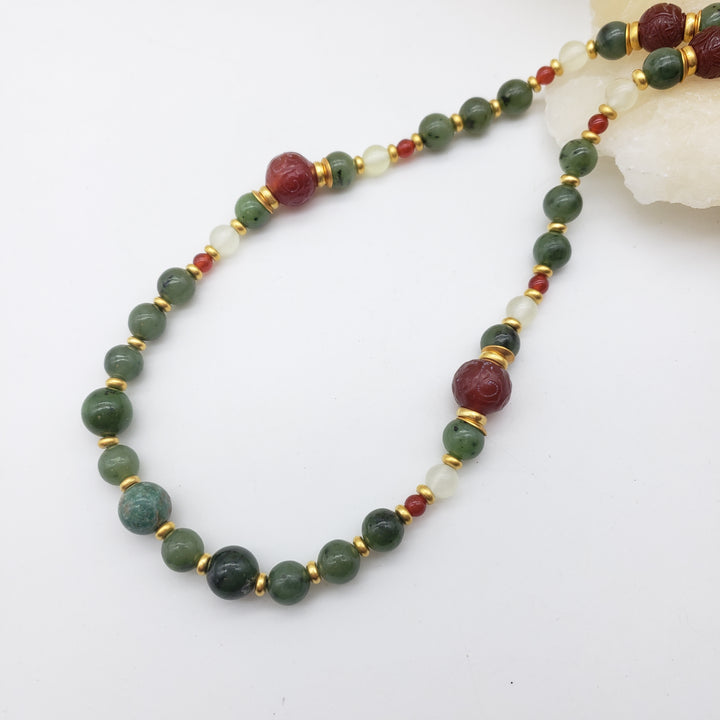 Beaded necklace with green, red, and gold beads on a white background
