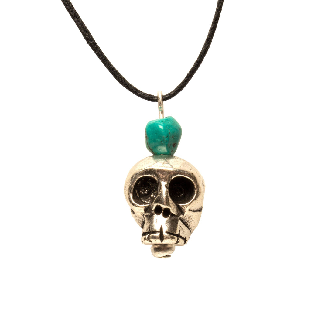 Skull-shaped pendant with a turquoise bead on a black cord against a white background