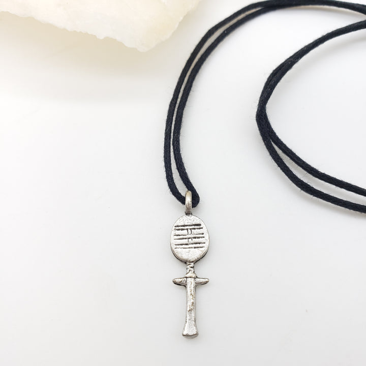 Black cord necklace with a silver akuaba doll pendant on a white background