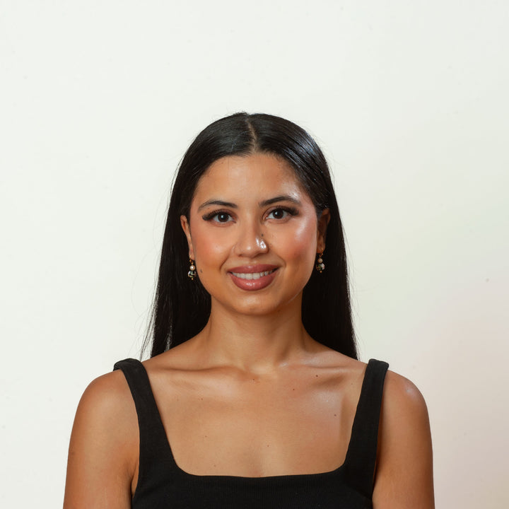 Woman with long dark hair wearing a black sleeveless top against a plain background