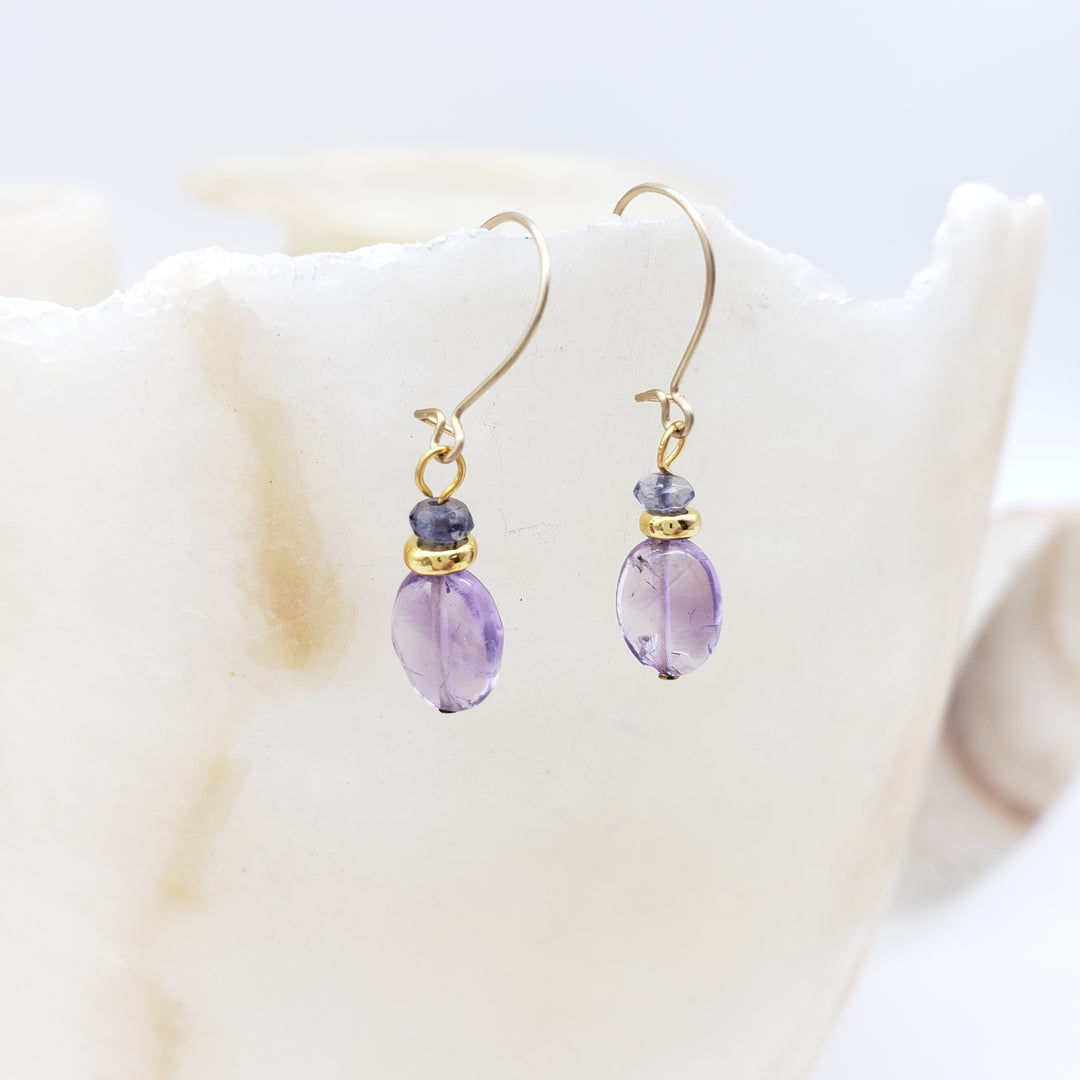 Gold earrings with purple beads on a white shell background