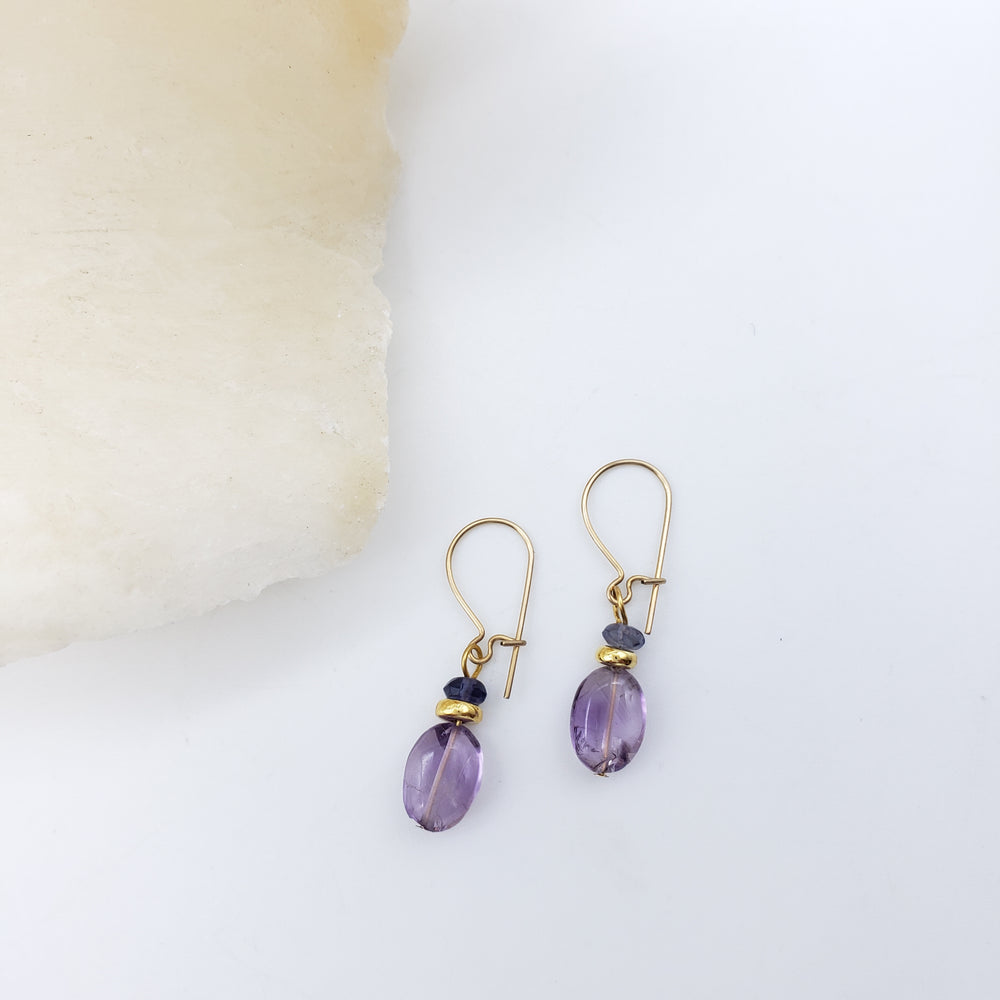 Pair of gold earrings with purple beads on a white background
