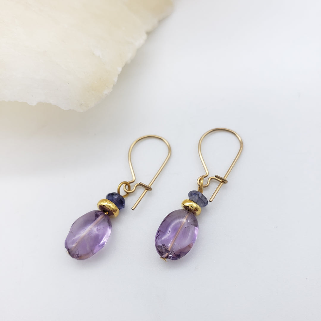 Pair of gold earrings with purple beads on a white background