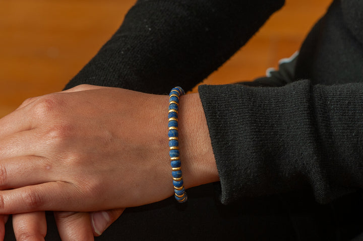 Hand wearing a blue and black bracelet on a wooden surface