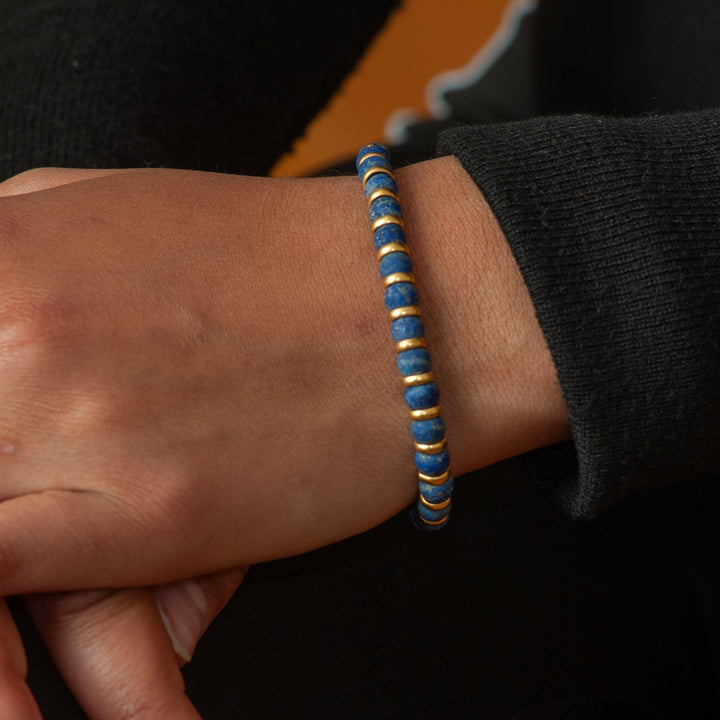 Close-up of a wrist wearing a blue and gold bracelet with a blurred background