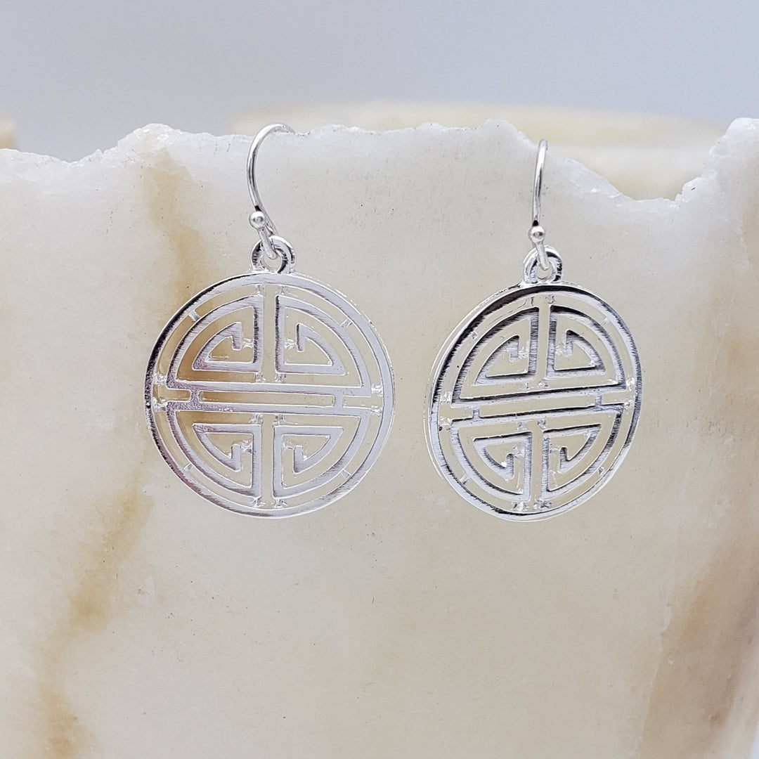 Silver earrings with circular design on a marble surface