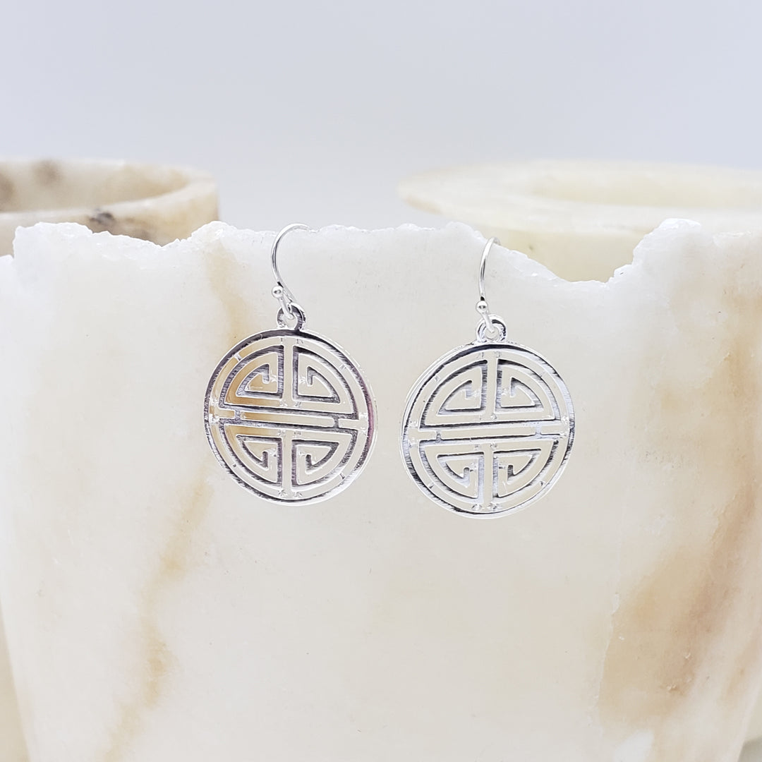 Silver earrings with a circular design on a white marble surface