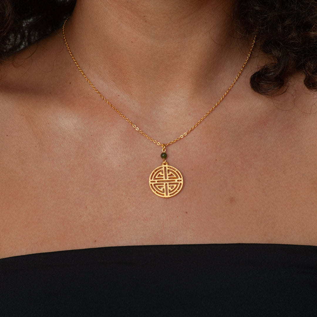 Gold necklace with a circular pendant on a person wearing a black top.