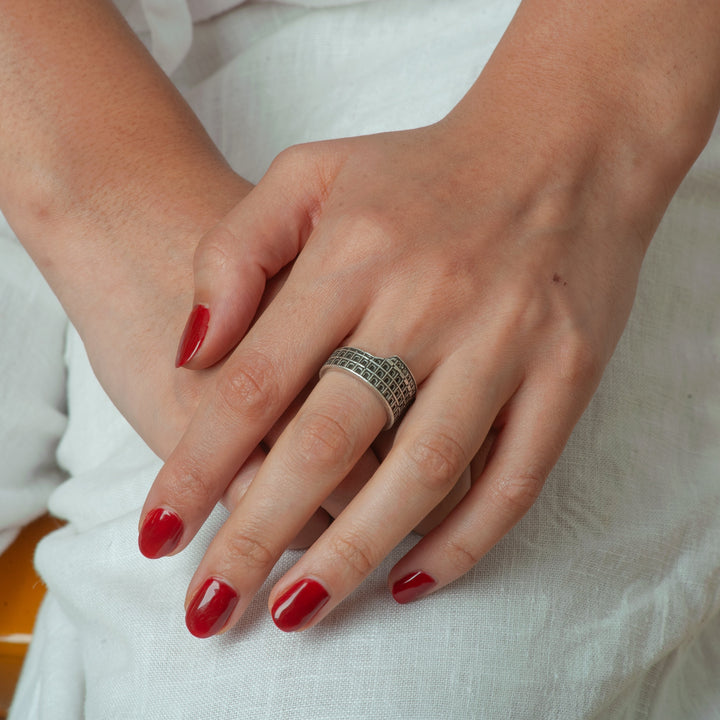 Close-up of a hand with red nail polish wearing a silver ring on a white background