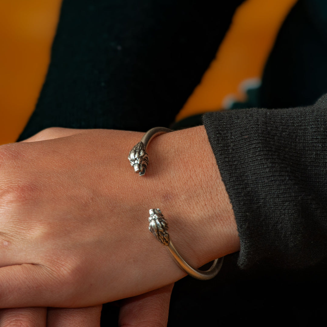 Close-up of a person's wrist wearing two silver bangles against an orange background
