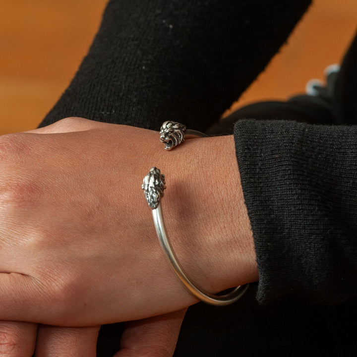Close-up of a person's wrist wearing two silver bracelets on a wooden surface.