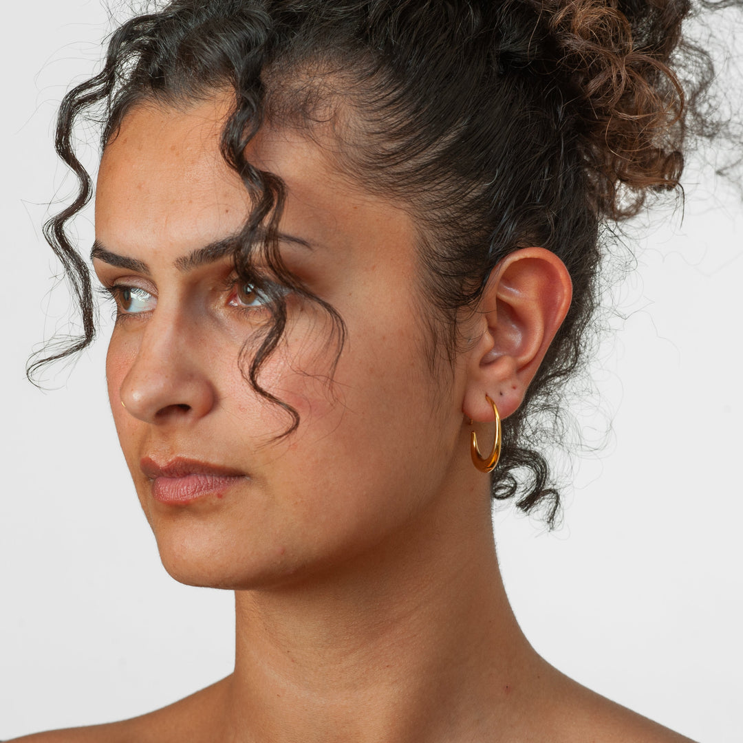Woman wearing a gold earring against a white background