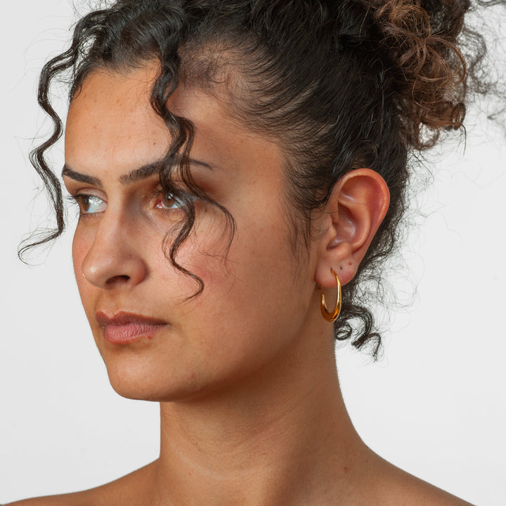Woman wearing a gold earring against a white background