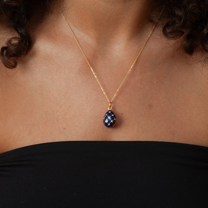 Person wearing a gold necklace with a blue pendant against a neutral background