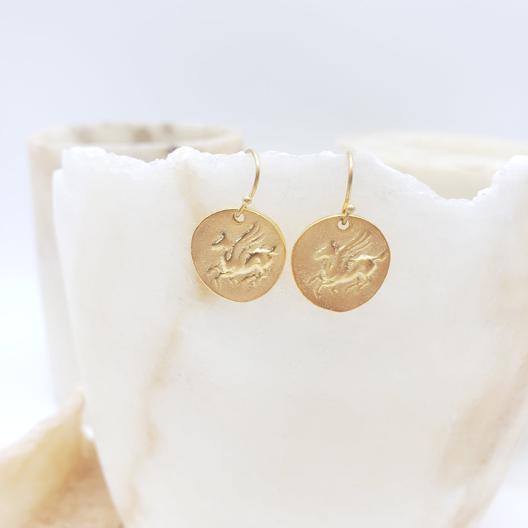 Gold circular earrings with engraved designs on a white background