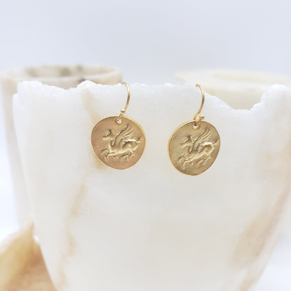 Two gold circular earrings with engraved designs on a white marble surface.