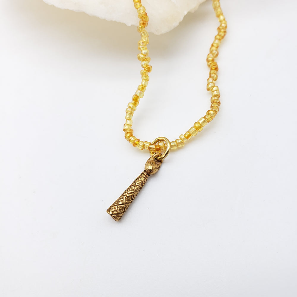A gold-toned beaded necklace with a textured geometric cat pendant, displayed on a clean white surface.