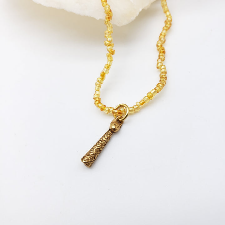 A gold-toned beaded necklace with a textured geometric cat pendant, displayed on a clean white surface.