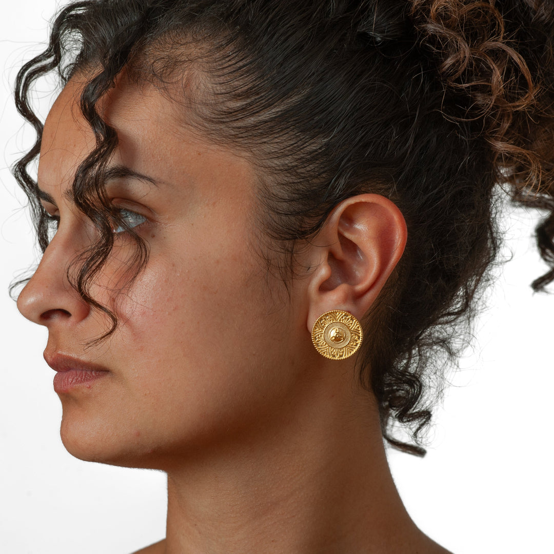 Close-up of a woman wearing gold earrings with a neutral background