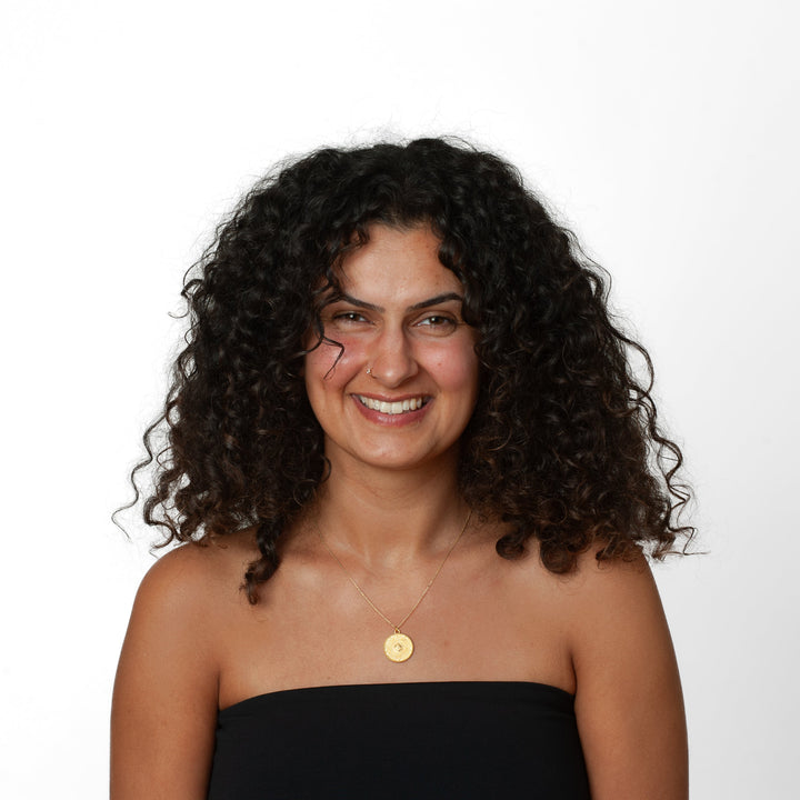Woman with curly hair wearing a black strapless top and gold necklace on a white background