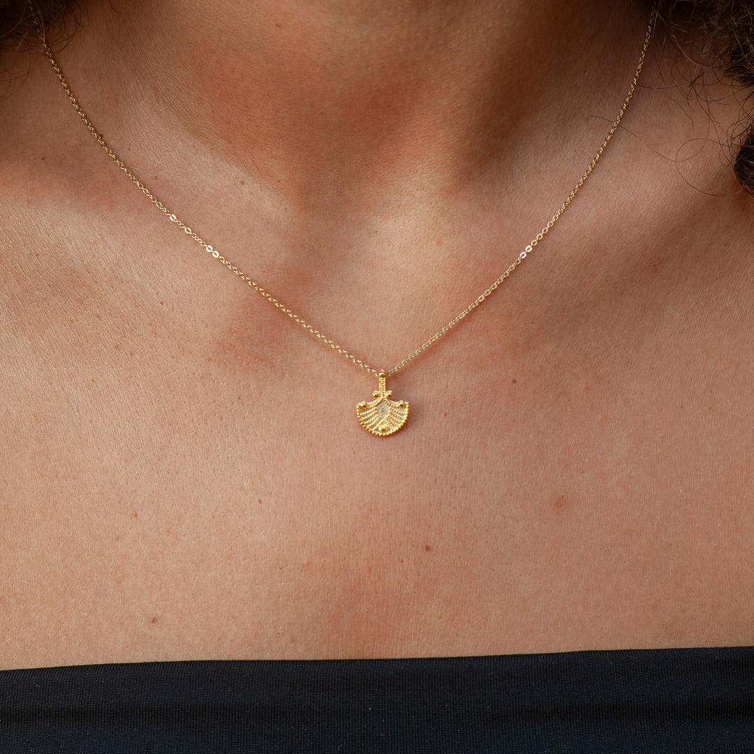 Gold necklace with a fan-shaped pendant on a person's neck
