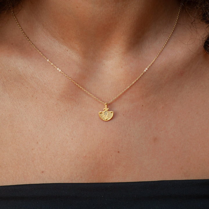 Gold necklace with a fan-shaped pendant on a person's neck