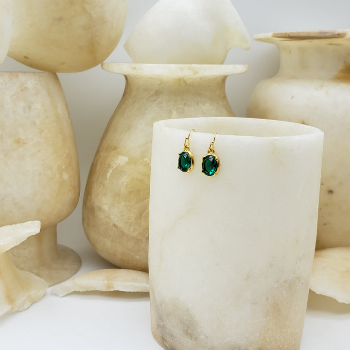 Gold earrings with green gemstones displayed on a white marble stand, surrounded by similar marble pieces.