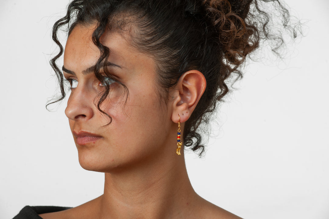 Close-up of a person wearing colorful earrings with a neutral background