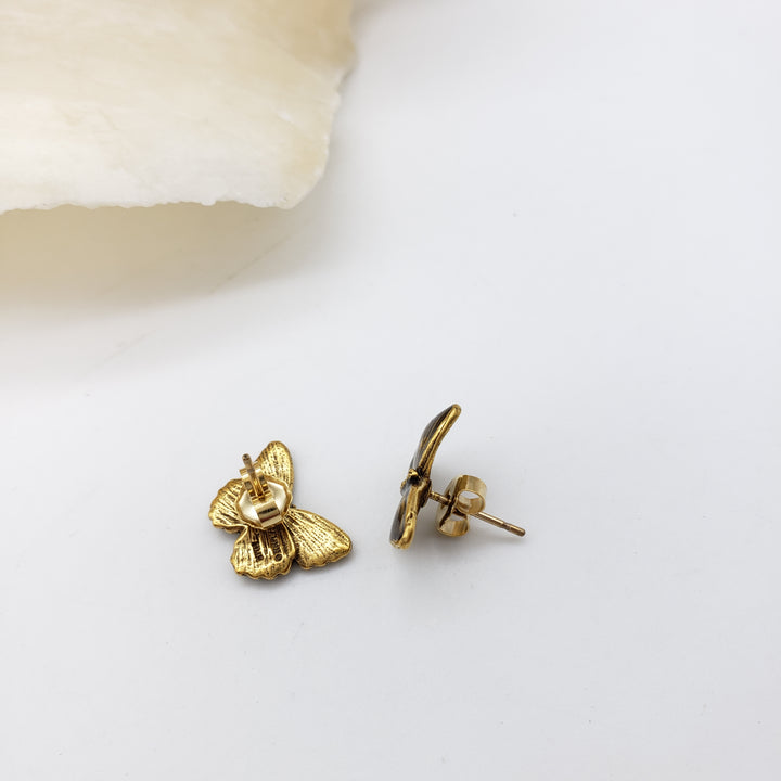A pair of small gold butterfly stud earrings on a clean white background, with one earring showing the butterfly front and the other showing the post and backing.